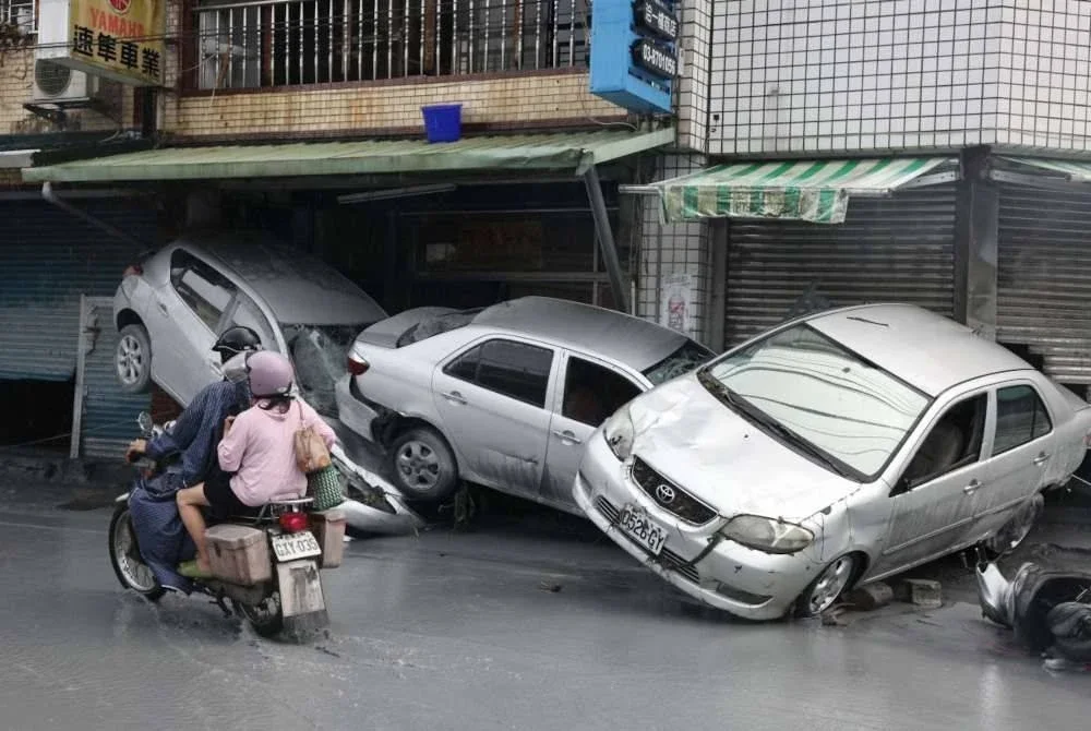 Penduduk menunggang motosikal melepasi kereta rosak yang dihanyutkan banjir di Hualien, Taiwan. Foto AFP