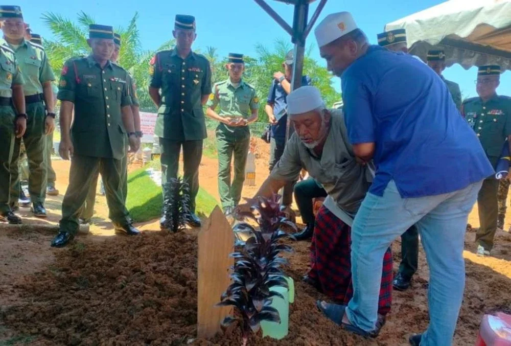 Bapa Allahyarham, Md Shariff Hashim, 68, dibantu anak ketiga, Mohd Shuhaimi menyiram air di pusara Mohd Ruzaini.