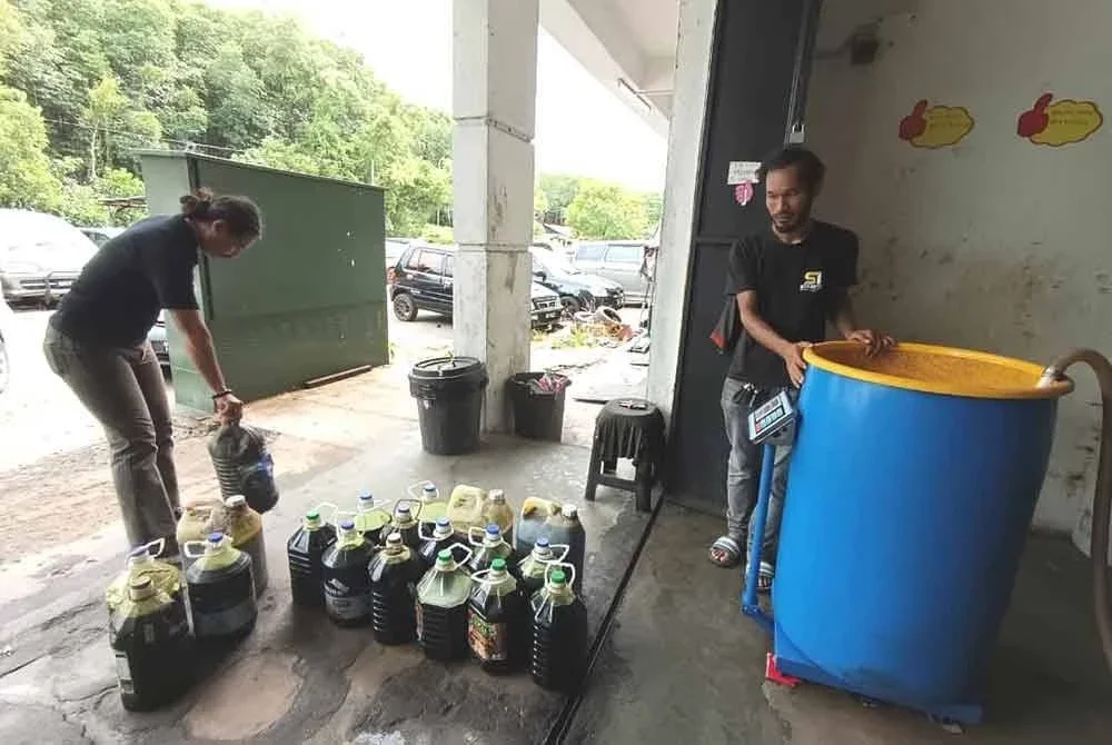 Muhammad Iman (kiri) menghantar minyak masak untuk dikitar semula di sebuah pusat pengumpulan di Kuala Ibai, Kuala Terengganu.