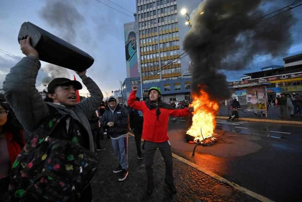 Penunjuk perasaan berkumpul di sebelah penghadang yang dibakar semasa tunjuk perasaan anti-kerajaan. Foto AFP