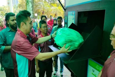 Mooi Lye (kiri) mencuba kaedah stesen pandu lalu untuk menyerahkan bahan kitar semula.