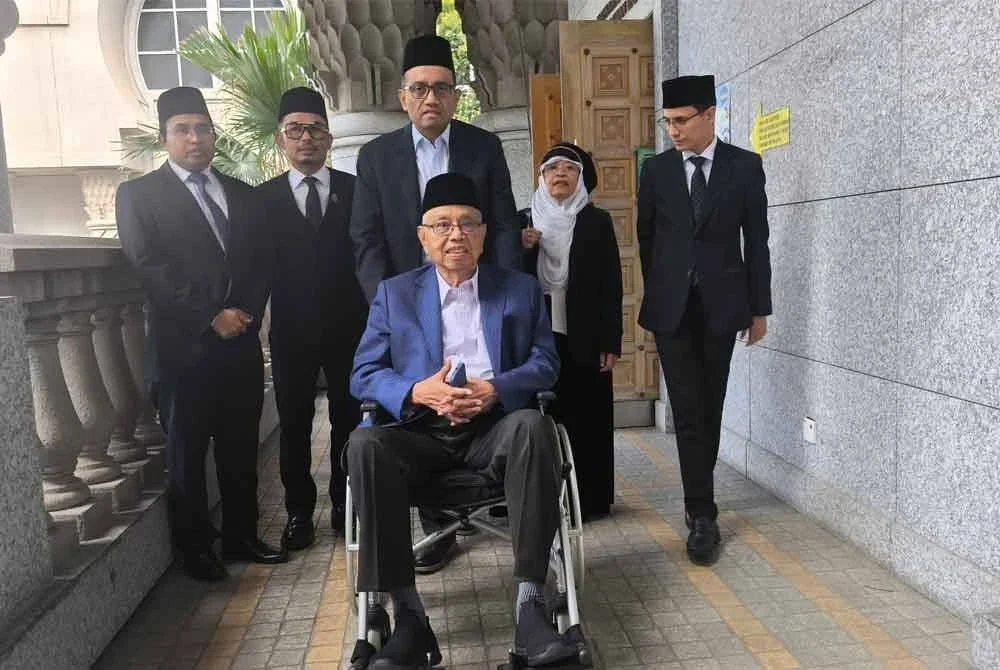 Shahriman (tengah) menolak kerusi roda dinaiki Shamsuddin ketika hadir ke Mahkamah Tinggi Syariah Putrajaya pada Khamis.