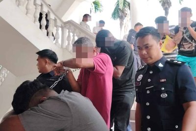Suspek (baju merah) diiringi anggota polis ketika dibawa ke mahkamah bagi mendapatkan perintah reman.