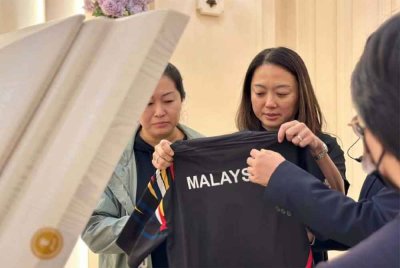 Hannah (dua kiri) memberi penghormatan kepada mendiang Shing Xuen dengan meletakkan jersi Team MAS di kerandanya sambil dibantu Lee Ping (kiri). - Foto ihsan FB Hannah Yeoh