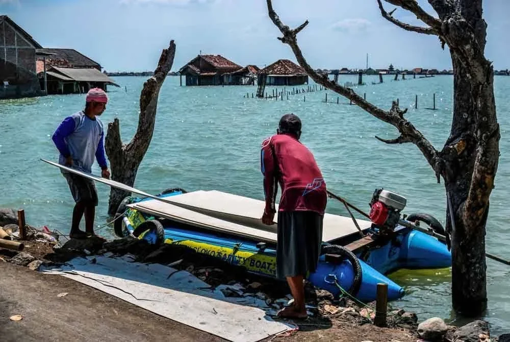 Penduduk perkampungan Bedono membawa bahan binaan dengan bot untuk meninggikan rumah masing-masing. - Foto AFP