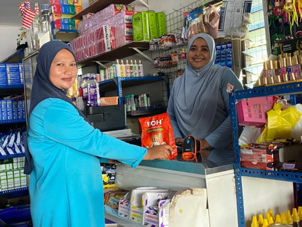 Nor Shamimie (kanan) melayan pelanggan di kedai runcitnya di Selising, Pasir Puteh.