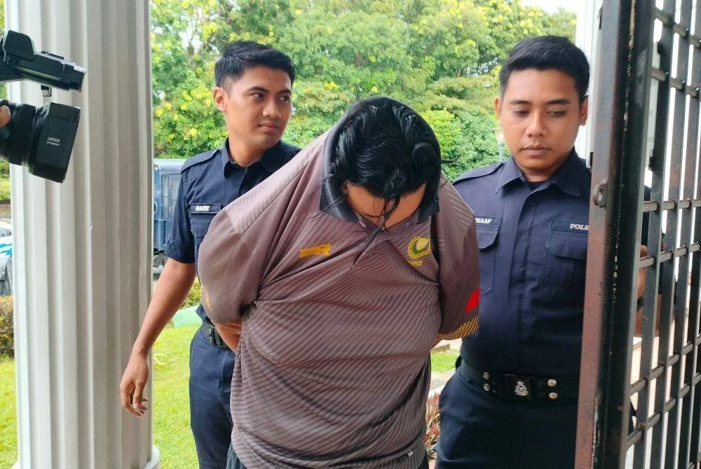 Tertuduh diiringi anggota polis ketika dibawa ke Mahkamah Balik Pulau, pada Jumaat.