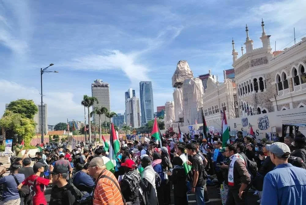 Kumpulan peserta himpunan Bantah Trump berkumpul di Dataran Merdeka, Kuala Lumpur dengan memegang plakad serta bendera Palestin pada Ahad. Foto Sinar Harian