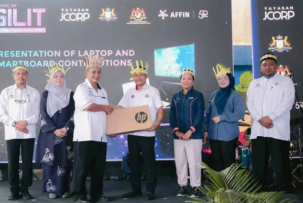 Aznan (empat dari kanan) menyampaikan komputer riba kepada wakil sekolah yang terlibat dalam Program Pendidikan Literasi Digital di SK Sayong Pinang, Kulai pada Isnin.