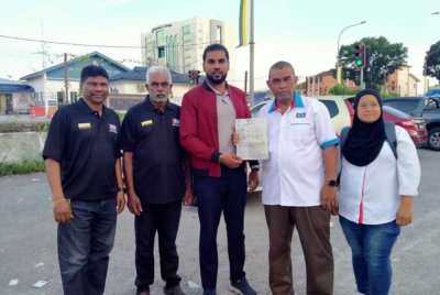 Kalaimughilan (tengah) menunjukkan laporan polis yang dibuat terhadap tindakan seorang individu memuat naik gambar menghina Anwar di IPD Ipoh pada Jumaat.