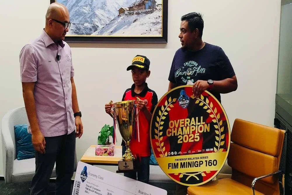 Al-Adam Mikail menunjukkan piala juara FIM MiniGP Malaysia 2025 kategori 160cc yang dimenangi kepada Fadzli (kiri) semasa majlis penyerahan sumbangan di PPSAS pada Isnin.