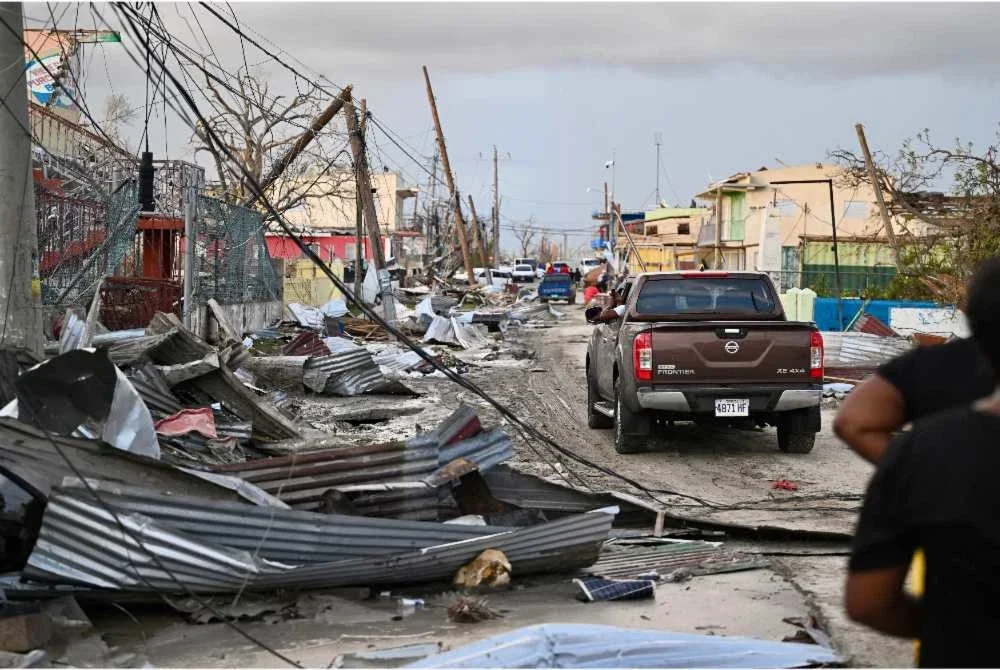 Sebuah kereta memandu melalui kawasan kejiranan yang musnah berikutan laluan Taufan Melissa di Black River, Jamaica pada 29 Oktober 2025. - Foto: AFP