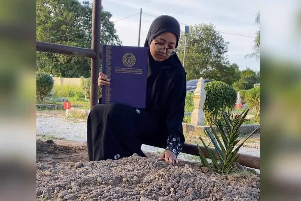 Dr Siti Ruqyah menggenggam erat ijazah yang baru diterima di sisi pusara ayahnya, Adnan di Tanah Perkuburan Islam Sri Aman, Pasir Puteh. Foto: SINAR HARIAN/HAZELEN LIANA KAMARUDIN