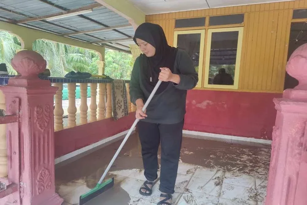 Shamiza membersihkan lumpur tebal yang memenuhi kediamannya di Kampung Sentosa, Sekinchan, pada Khamis.
