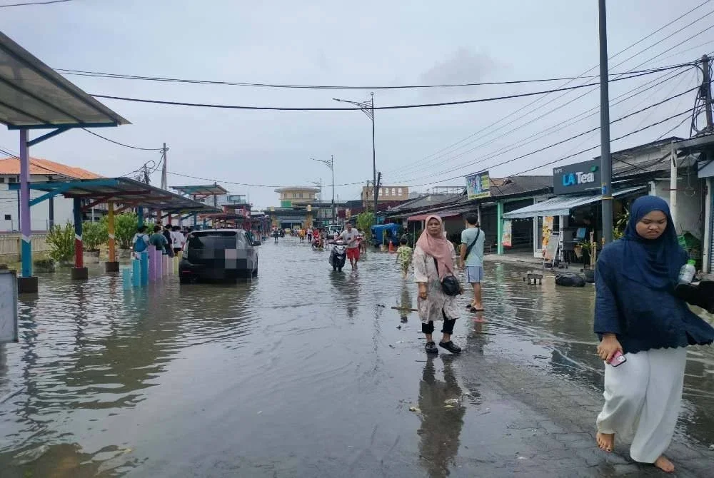 Orang ramai meredah air pasang besar di laluan utama Pekan Kukup. 