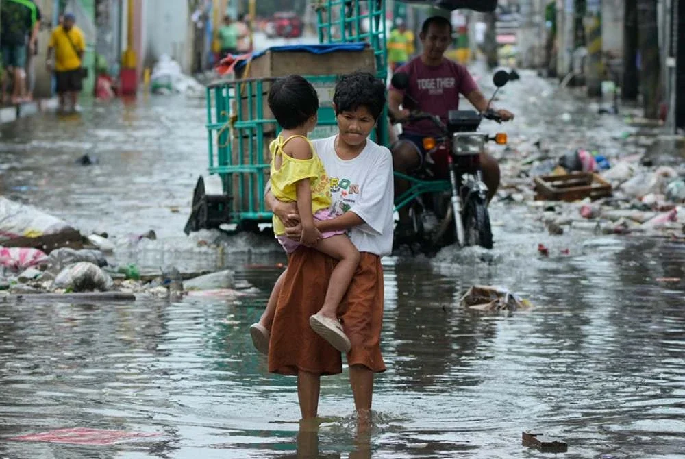 Seorang wanita bersama anaknya meredah jalan yang dinaiki air akibat Taufan Fung-wong dan fenomena air pasang besar. Foto AP
