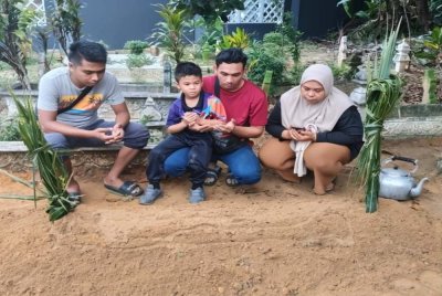 Muhammad Saiful (tengah) bersama anaknya membacakan doa di hadapan pusara Nor Fadillah yang meninggal dunia pada Rabu selepas tujuh tahun terlantar sakit.
