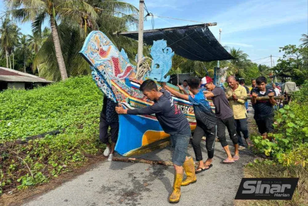 Nelayan dan penduduk beramai-ramai menolak perahu di atas ‘landasan’ kayu bakau. - Foto: SINAR HARIAN/ADILA SHARINNI WAHID