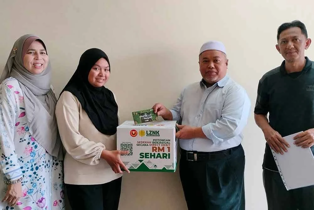 Ahmad Mustaqim menyampaikan sumbangan kepada Madihah Izzati Atiqah sambil disaksikan Natipah (kiri).