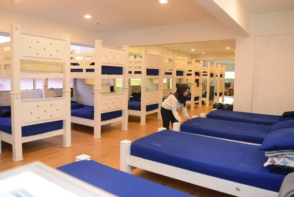 Seorang pekerja sedang mengemas katil yang disediakan untuk kemudahan keluarga yang menginap dorm penginapan sementara itu.