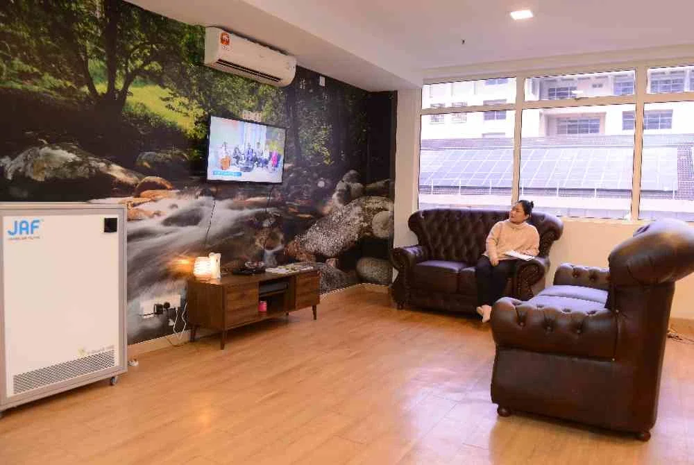 Seorang waris pesakit meluangkan masa menonton televisyen di ruang rehat Better Brighter Dormitory yang dilengkapi penyaman udara dan perabot selesa.