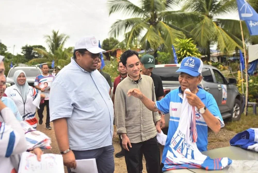 Hassan (kanan) menggantikan baju dan topi BN dengan pakaian GRS selepas mengisytiharkan keluar BN, disaksikan Hazem (tiga dari kanan) di Kampung Luboh, Libaran pada Khamis.