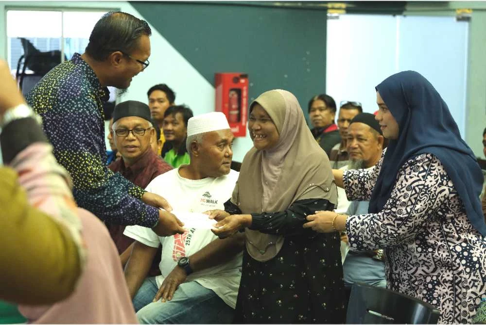 Muhtar (kiri) menyampaikan sumbangan zakat kepada salah seorang penerima pada majlis agihan zakat yang diadakan di Dewan Serbaguna EPIC Berhad di Kemaman pada Khamis