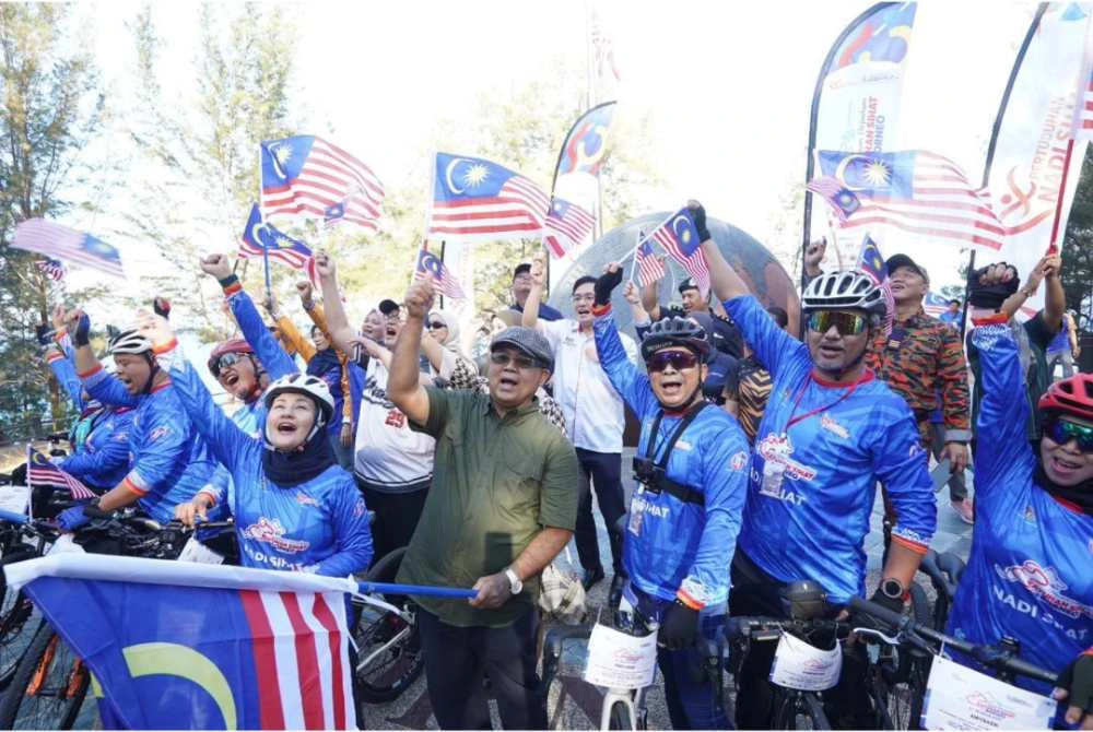 Aaron (tengah) bersemangat mengibarkan Jalur Gemilang bersama warga komuniti sempena program perpaduan yang dianjurkan bagi menyemai semangat kebersamaan dan cintakan negara.