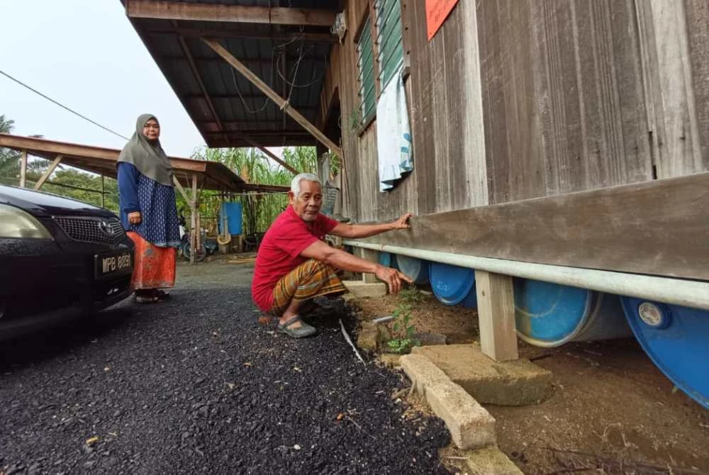 Pok We menunjukkan antara tong plastik berwarna biru yang diikat di bahagian bawah rumah untuk mengapungkan rumah tersebut.