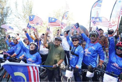 Aaron (tengah) bersemangat mengibarkan Jalur Gemilang bersama warga komuniti sempena program perpaduan yang dianjurkan bagi menyemai semangat kebersamaan dan cintakan negara.