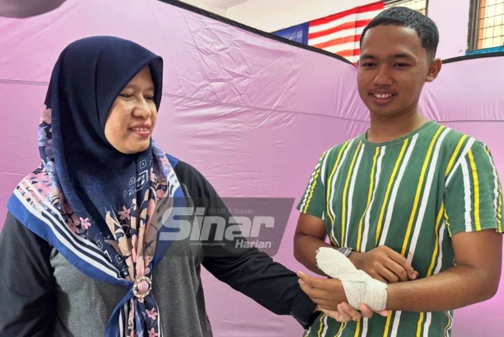 Ibunya, Nor Azizah Ibrahim (kiri) memegang perlahan tangan kiri Che Mohd Hanif Haikal yang cedera.