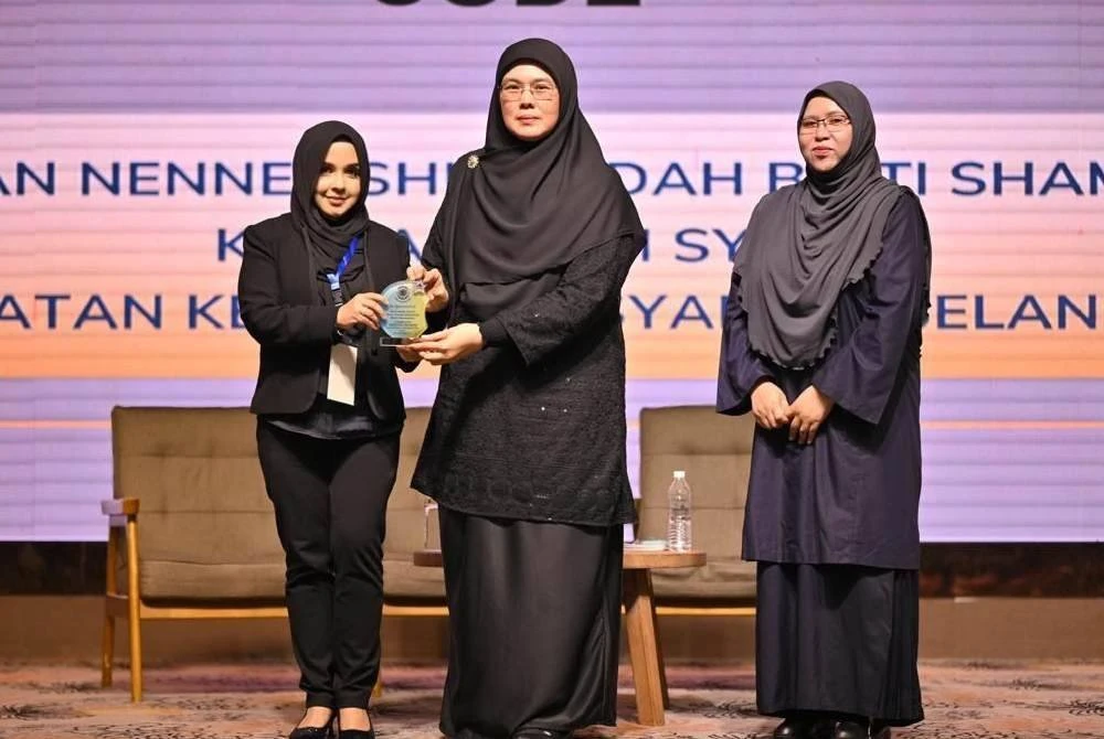 Nurul Muhaniza (kiri) menyerahkan cenderamata kepada Ketua Hakim Syarie Selangor, Nenney Shuhaidah Shamsuddin (tengah) pada Forum dan Hi-Tea Pengamal Konveyans Selangor.