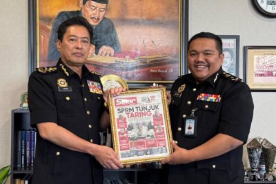 Azam (kiri) menunjukkan paparan akhbar muka depan Sinar Harian yang dibingkaikan sebagai tanda penghargaan.