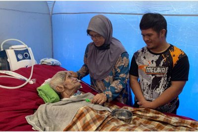 Che Sarimah ditemani Muhammad Arif (kanan) menjaga suaminya Abdullah yang terlantar disebabkan strok sejak tiga tahun lalu ketika ditemui PPS Sekolah Kebangsaan Parang Puting - Foto: Bernama