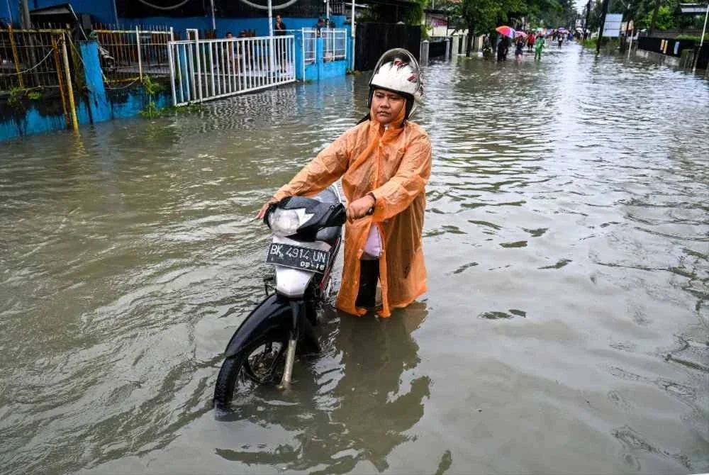 Seorang wanita menolak motosikalnya melalui jalan yang ditenggelami banjir di Medan, Sumatera Utara, Indonesia.-AFP