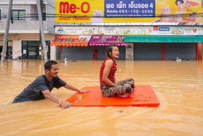 Seorang lelaki membantu memindahkan seorang wanita melalui banjir di Hatyai, wilayah Songkhla, selatan Thailand.-AFP