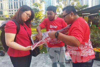 Zamri (kanan) menyantuni pembaca Sinar Harian di LRT Ampang Park pada Isnin.