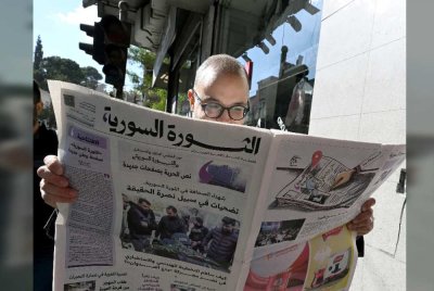 Seorang lelaki di Damsyik tekun membaca kandungan akhbar al-Thawra al-Souriya. Foto AFP