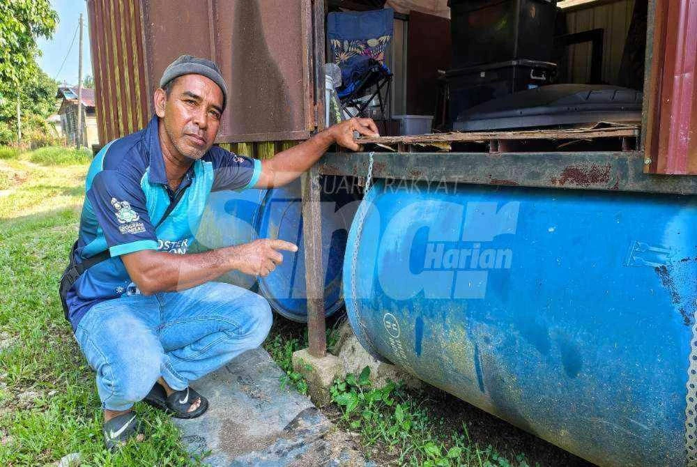 Husain menunjukkan tong biru yang dipasang pada rumah rakit. - Foto Sinar Harian