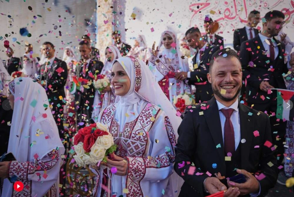Pasangan Eman Hassan Lawwa dan Hikmat Lawwa, masing-masing berusia 27 tahun, berjalan berpegangan tangan mengenakan pakaian tradisional Palestin dan sut sambil melalui runtuhan bangunan di selatan Gaza, bersama deretan 54 pasangan lain yang melangsungkan perkahwinan beramai-ramai pada Selasa.-Agensi