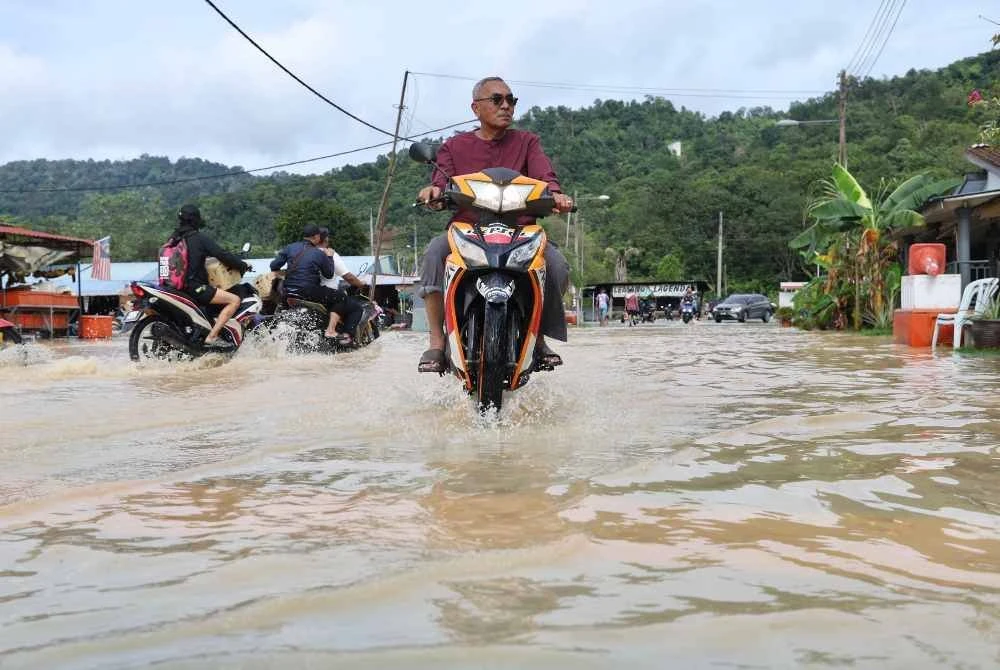 Penduduk meredah banjir di jalan utama di Kampung Sungai Serai. - Bernama