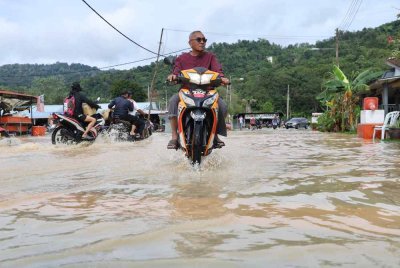 Penduduk meredah banjir di jalan utama di Kampung Sungai Serai. - Bernama