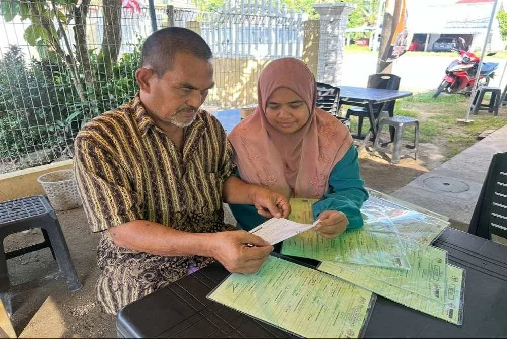 Shaharuddin (kiri) dan isterinya, Nur Mariani Abdul Rahmah (kanan) melihat slip permohonan kad pengenalan terkini. Foto Sinar Harian/ Adila Sharinni Wahid