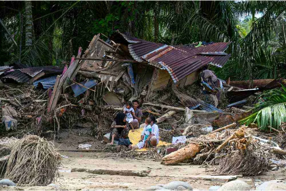 Sebuah keluarga duduk di luar rumah mereka yang musnah akibat banjir.