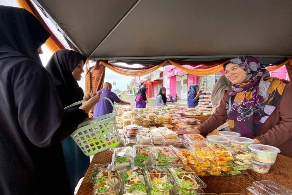 Maziah (kanan) sibuk melayan pelanggan yang ingin mendapatkan makanan berharga RM3 sepeket di Vendor Mami, Pasir Puteh pada Sabtu. Foto Sinar Harian/Hazelen Liana Kamarudin