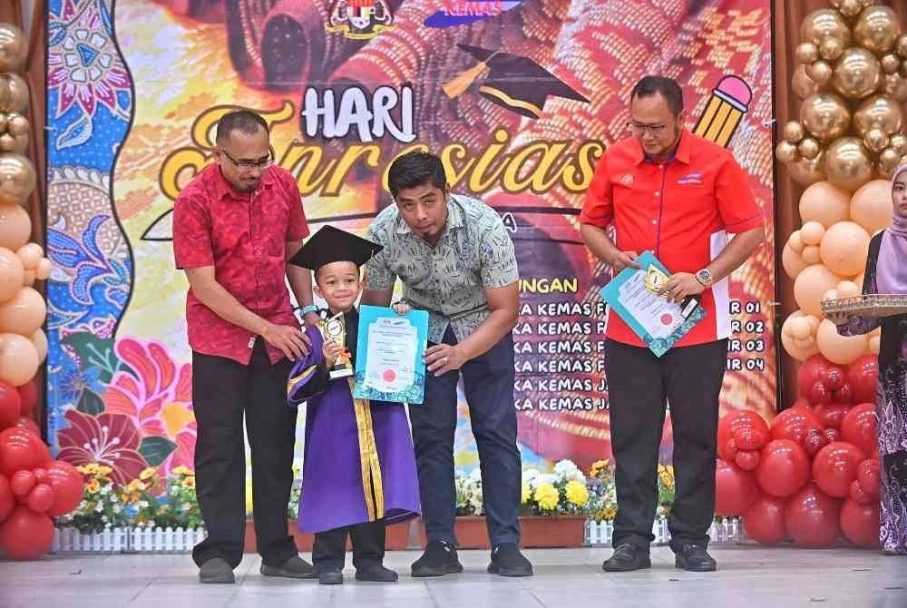 Faisal (kanan) mengiringi Mustaqim menyerahkan sijil kepada seorang kanak-kanak pada Majlis Apresiasi Tabika KEMAS Felda Lepar Hilir 1 hingga 4 dan Tabika KEMAS Kampung Orang Asli Batu 14 dan Kilometer 56, pada Sabtu.