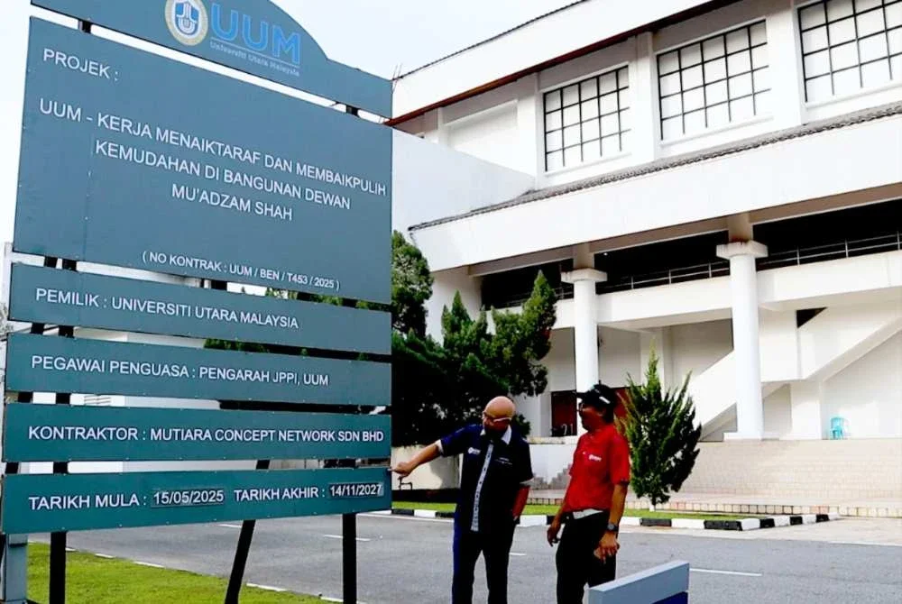 Ahmad Martadha (kiri) menunjukkan papan tanda Dewan Mu’adzam Shah terlibat dalam projek menaik taraf dan membaik pulih infrastruktur, termasuk penggantian bumbung, yang dijadualkan bermula 14 Mei 2025 hingga 14 November 2027.