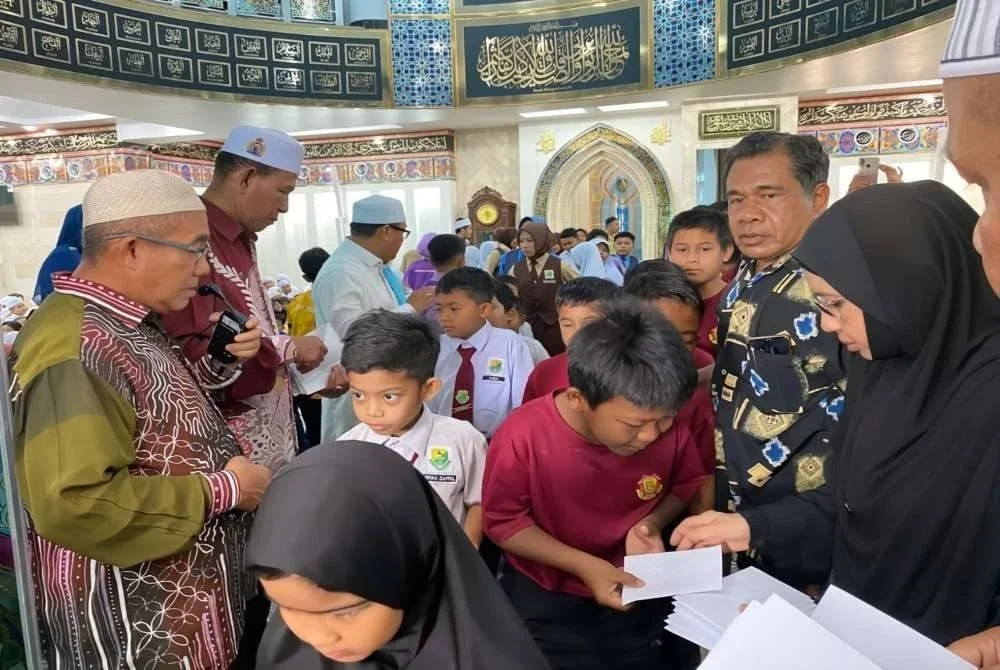 Ibrahim (kiri) dan Rohani (kanan) mengagihkan sumbangan kepada para pelajar.