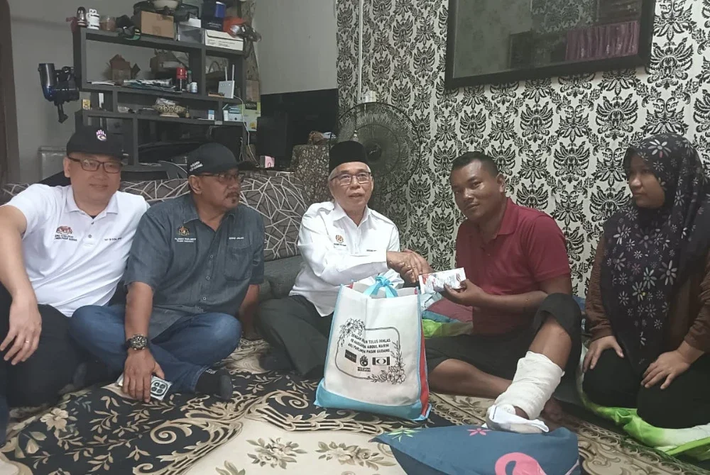 Hassan (tengah) menyampaikan bantuan kepada Korperal Abdul Halim Nasir, anggota Balai Polis Permas Jaya yang terlibat dalam kemalangan di kediamannya di Bandar Seri Alam pada Isnin.