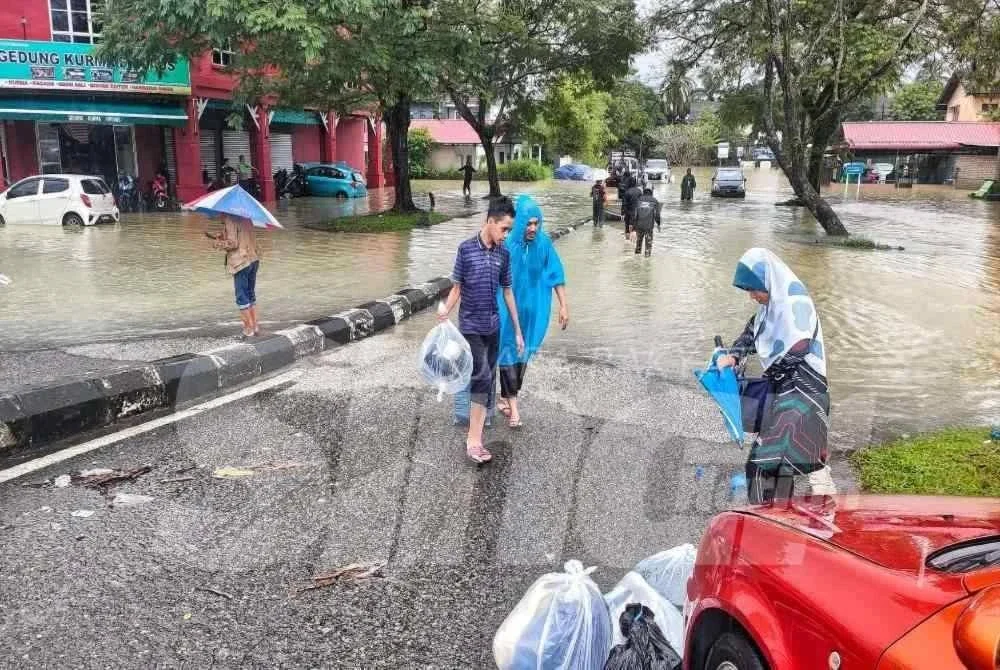 Penduduk di Taman Guru membantu barang selepas meredah air banjir di kawasan terbabit. 